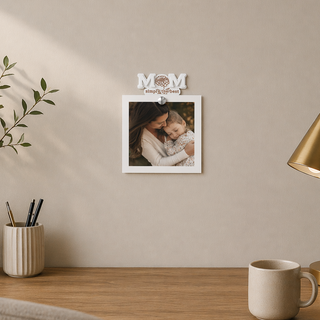 Decorative wall frame with a photo of a woman and child, placed on a wall above a wooden surface with a lamp and plant.