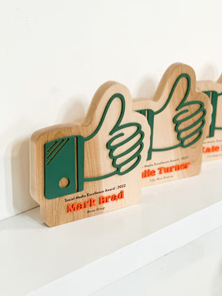 hardwood awards in the shape of a thumbs up with layered painted wood and engraved details on maple wood