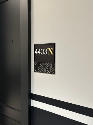 black acrylic sign with a cut out design, raised white acrylic numbers and a raised gold acrylic letter