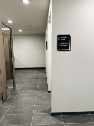 black acrylic directional sign with raised white acrylic lettering and arrows pointing to lockers, sauna, restrooms, showers