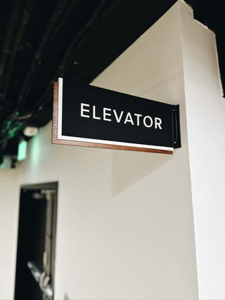 elevator wayfinding sign made from black acrylic with raised white acrylic letters and a wood border