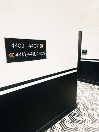 black acrylic directional sign with raised white acrylic room numbers and gold arrows 