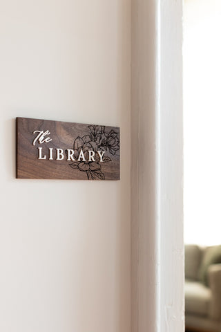 custom wayfinding rectangular wood sign with engraved floral details and raised white acrylic lettering "the library"