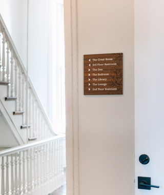 custom wayfinding square wood sign with engraved floral details and white text and arrows 