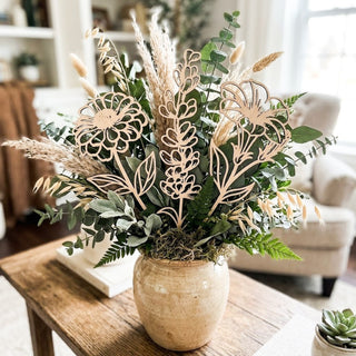 Decorative plant arrangement with wooden leaf accents on a wooden table in a living room.