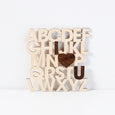 alphabet letters stacked up 5 rows, cut out in light wood with i heart u highlighted in dark wood aligned with the alphabet, laid against a white wall