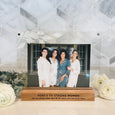 "heres to strong women, may we know them, may we be them, may we raise them" engraved in black ink on a wood base with two pieces of engraved acrylic with leaves at the top left corner holing up a family photo of a mom and her three daughters. The frame comes in various sayings